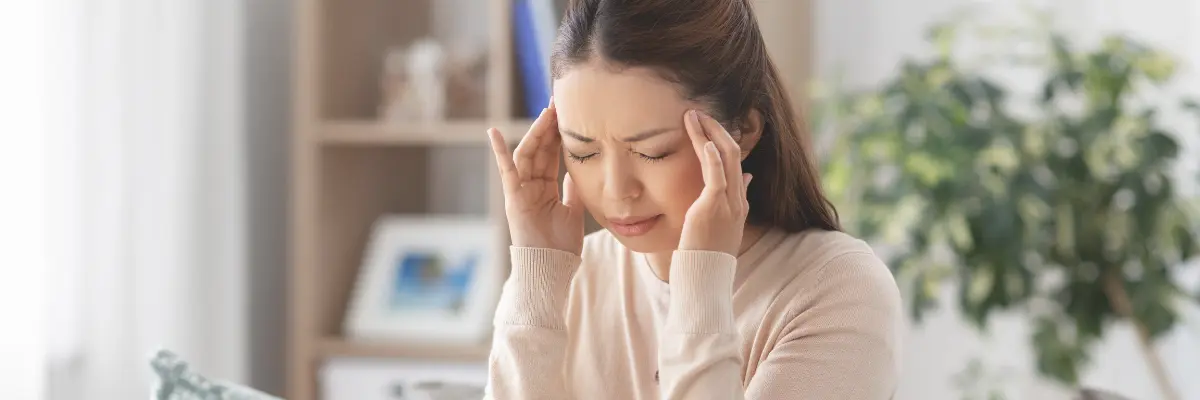 「こめかみを押さえて頭痛に悩む女性のイメージ（名古屋市千種区本山 テソラ治療院）」