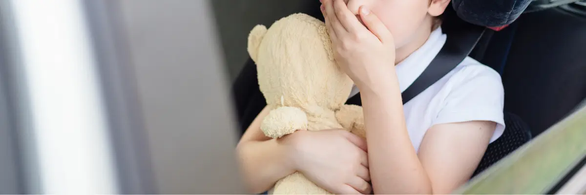 車の座席で顔を覆い、乗り物酔い（吐き気・不快感）に耐える子供の様子